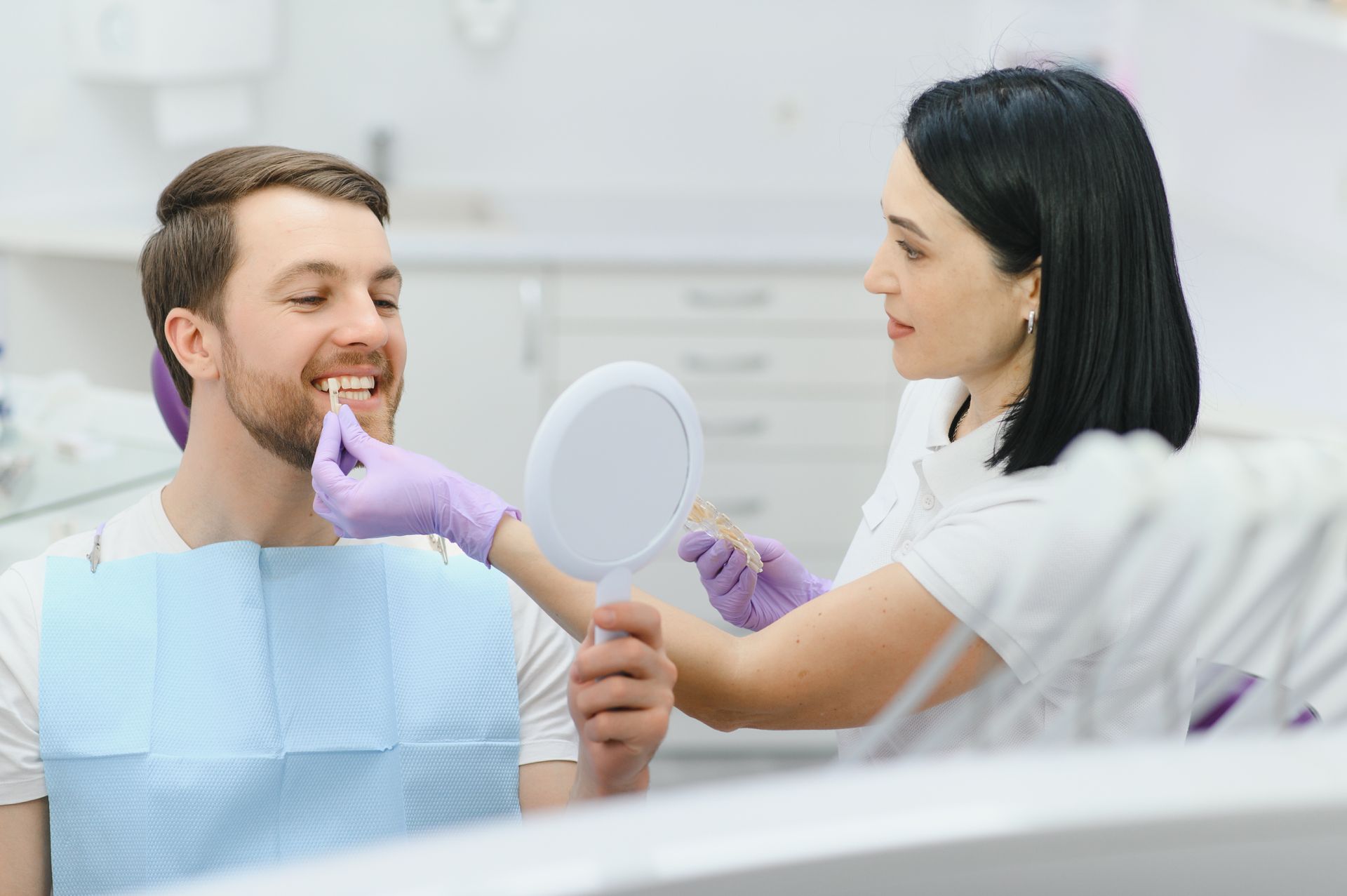 Dentist examining a patient’s teeth with a mirror while another clinician assists in a bright dental clinic