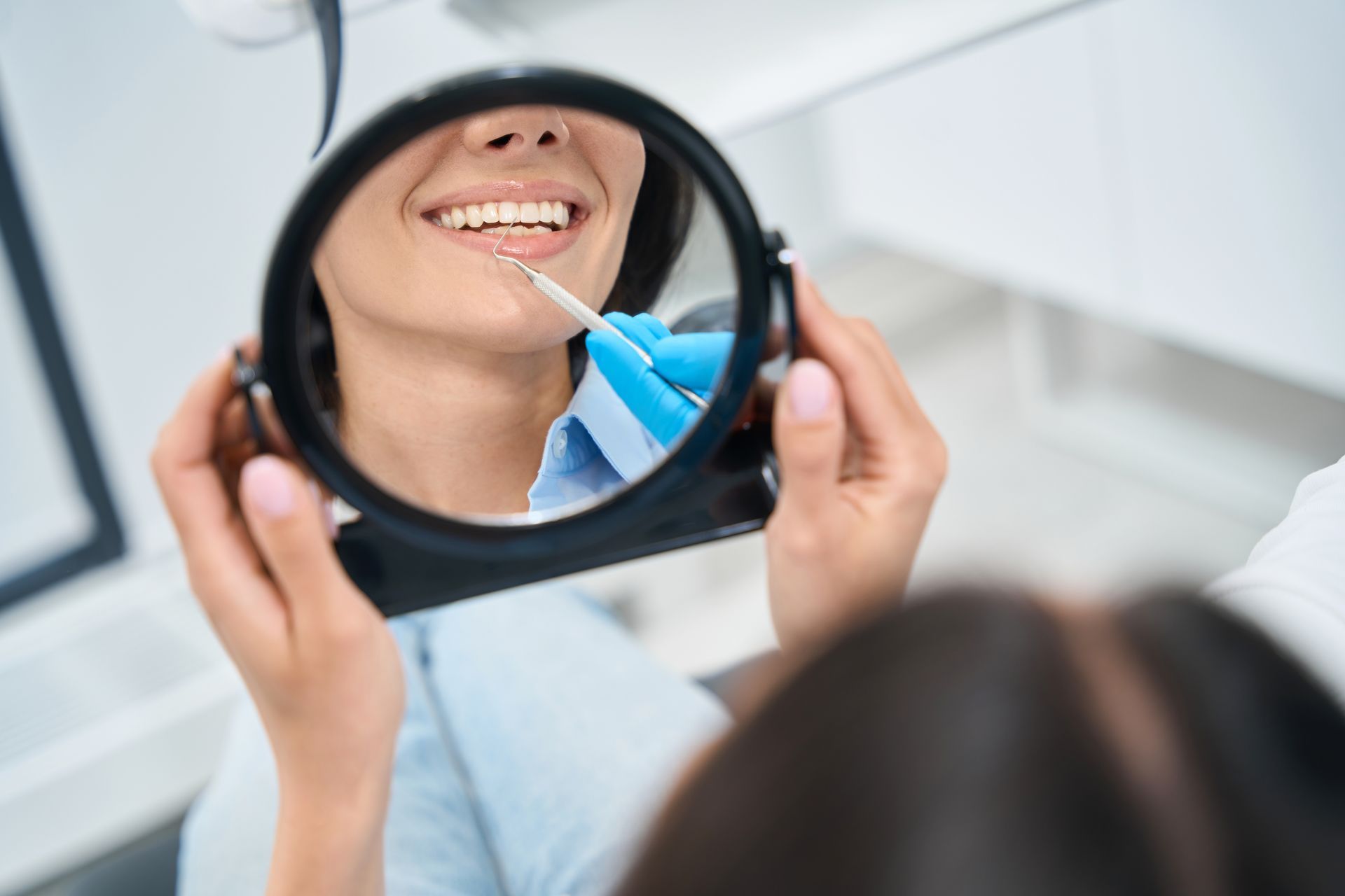 Patient smiling in a dental mirror while a dentist applies treatment with a blue tool