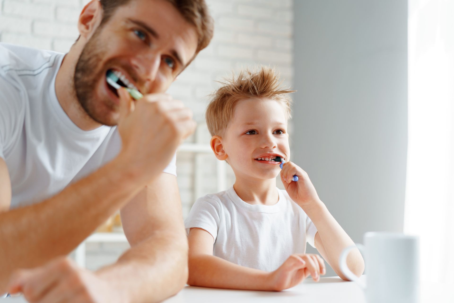 Two people brushing their teeth in a bright bathroom, one adult and one child.