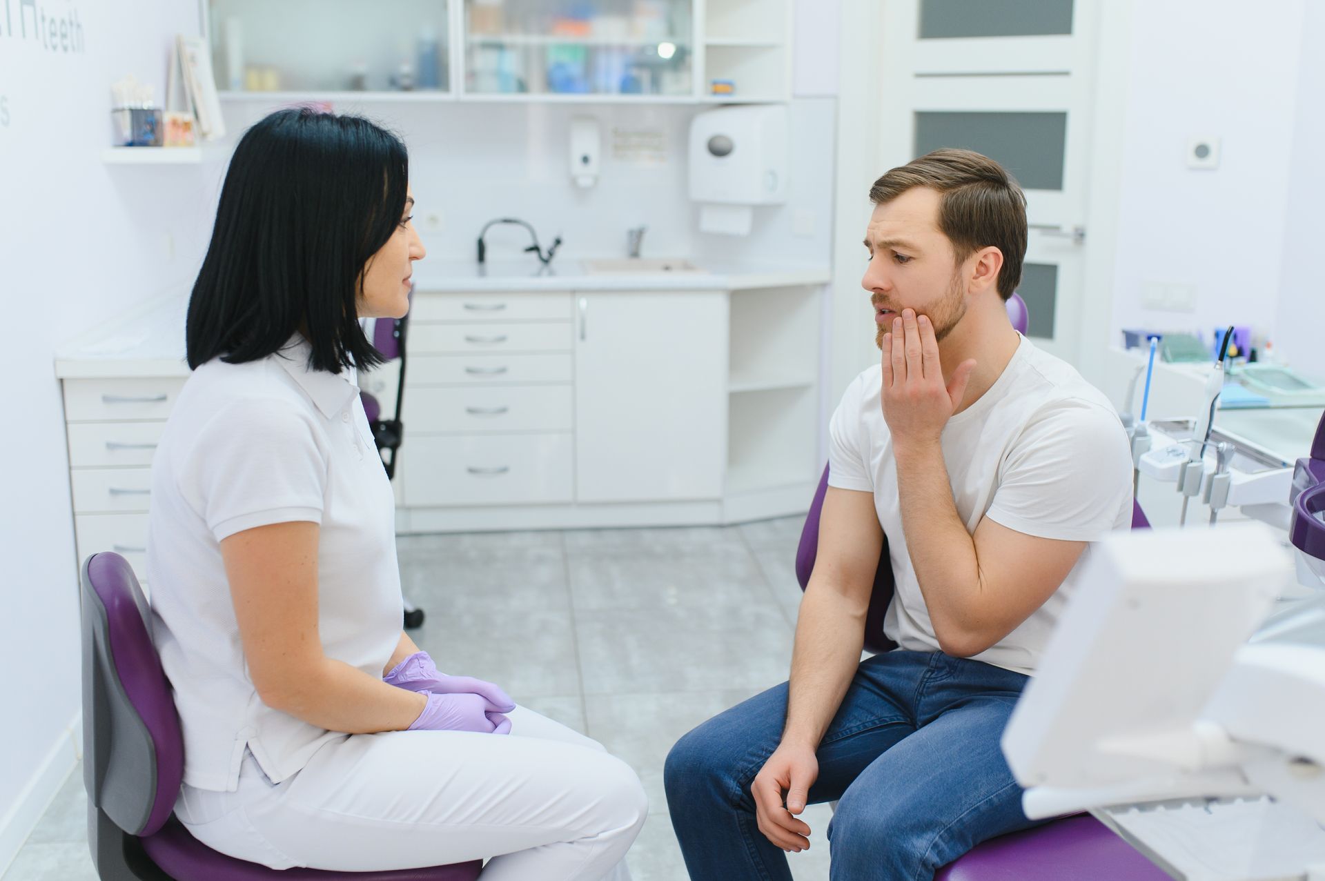 Patient and dentist talking in a bright dental clinic, with the patient touching his cheek.