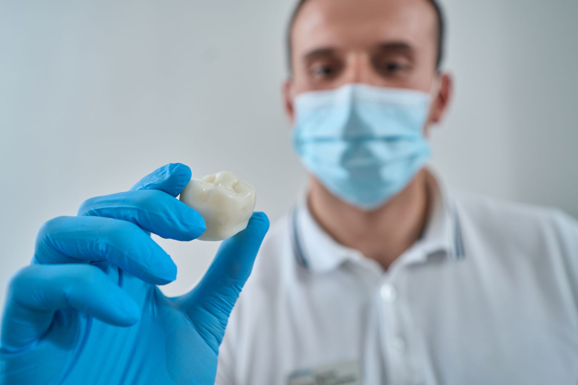 Gloved researcher holding a tooth model while wearing a surgical mask in a lab or clinical setting