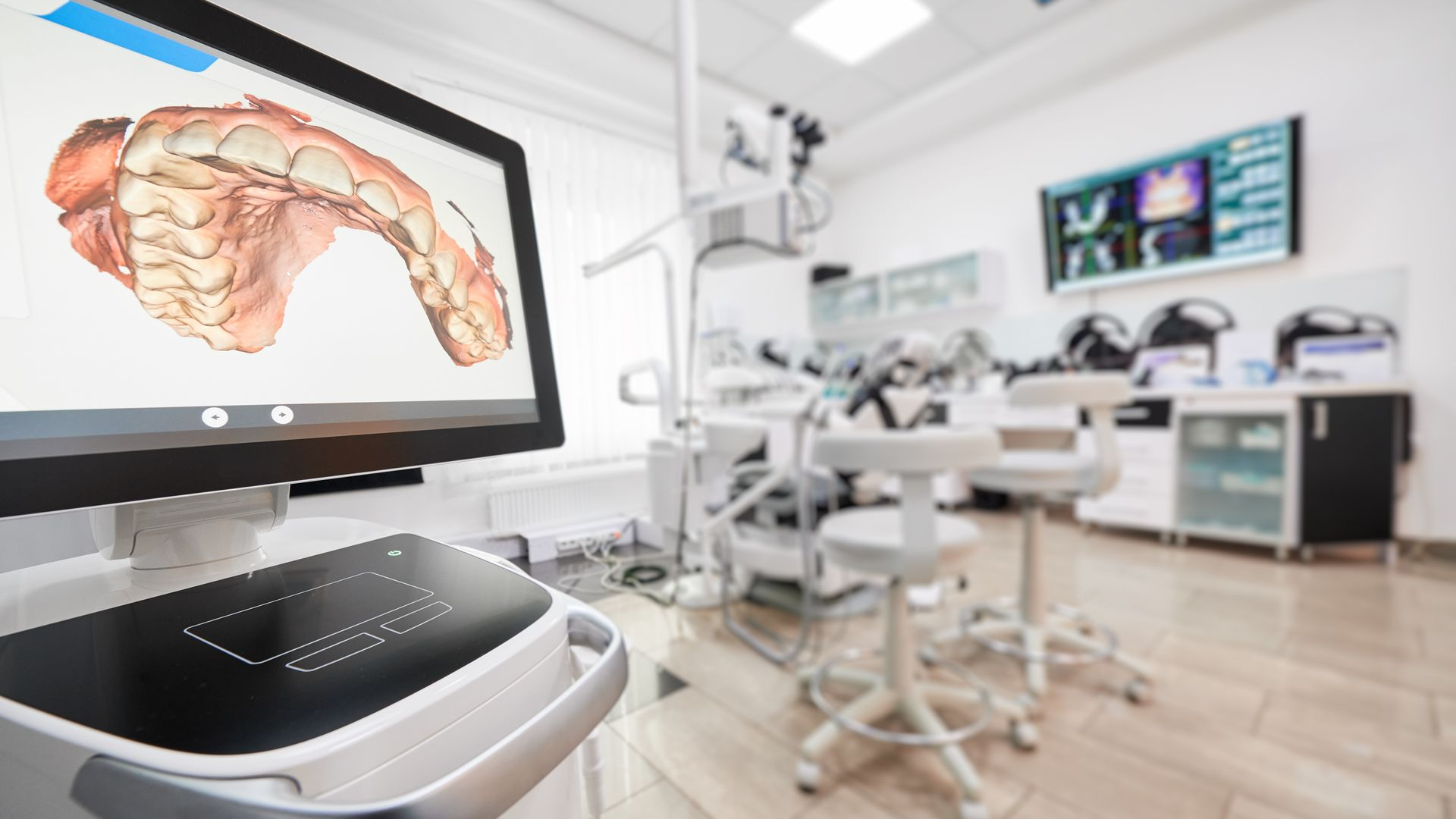 Dental office with a computer displaying a 3D dental scan, and dental equipment in the background.