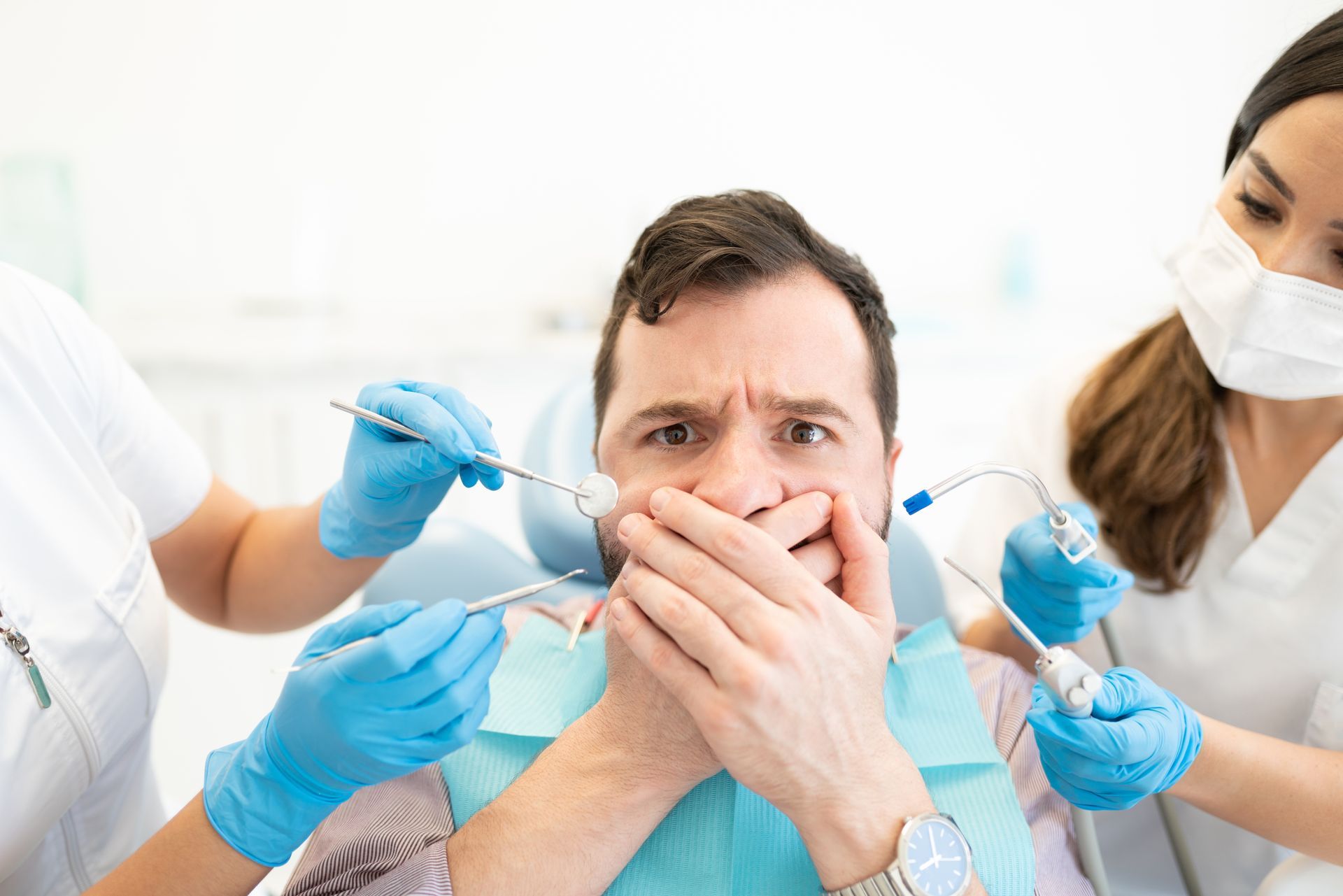 Dentist treating a startled patient while two assistants use dental tools and gloves