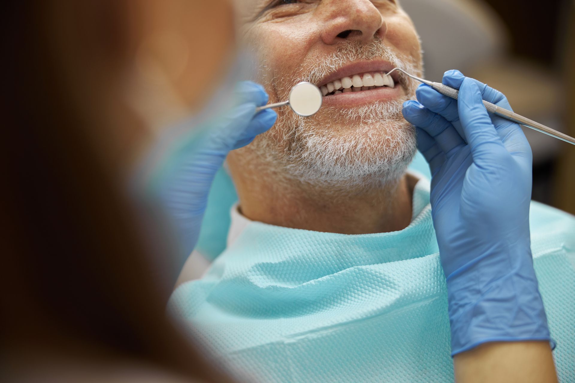 Dentist examining a smiling patient’s teeth with gloves and dental mirror