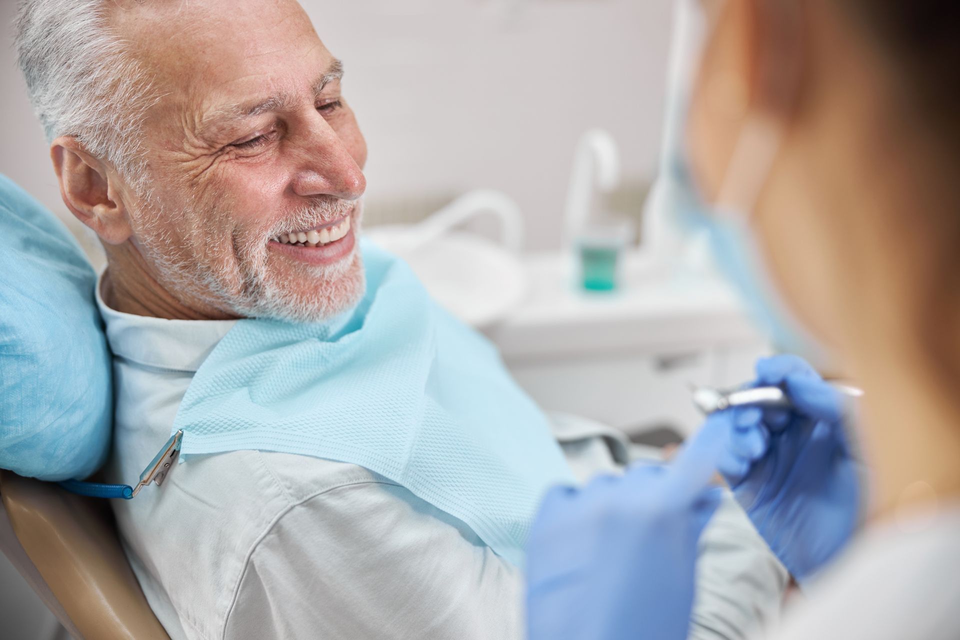 Dental patient smiling as a dentist examines his teeth with blue gloves in a clinic
