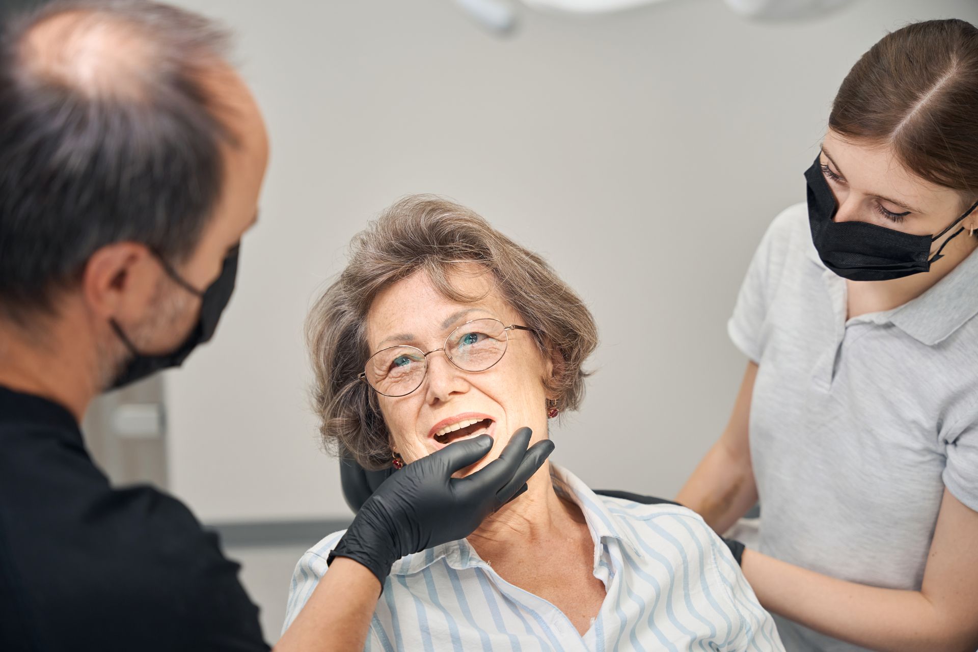 Dentist examining a patient while an assistant stands nearby in a clinic