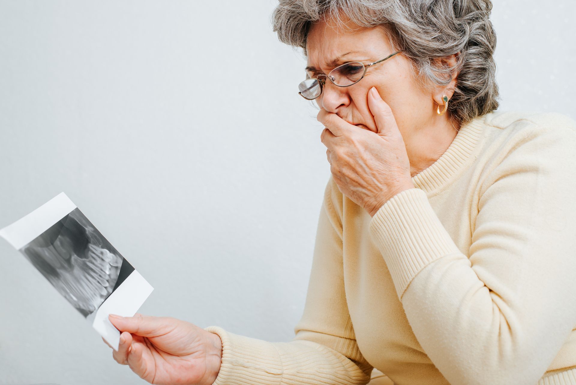 Woman holding an X-ray and covering her mouth with concern against a light background