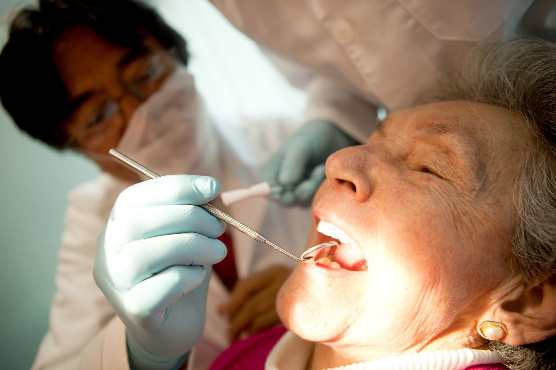 Dentist examining a patient’s open mouth with a dental mirror and gloved hand