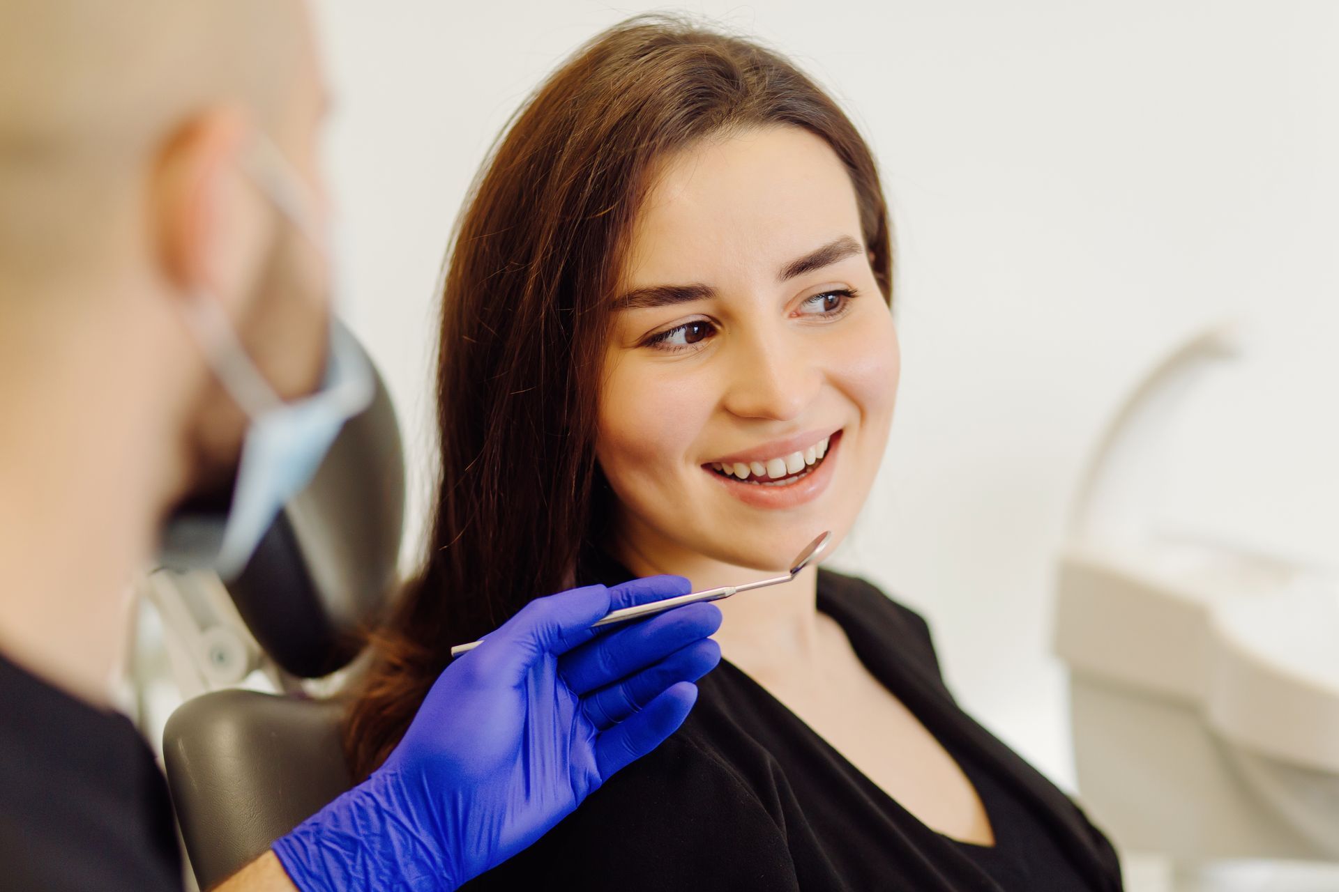 Dentist in blue gloves examining a smiling patient in a dental chair