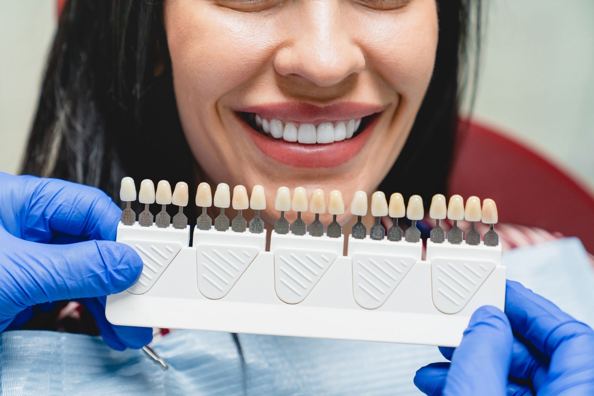 Dentist holding a teeth shade guide next to a patient's smiling teeth.
