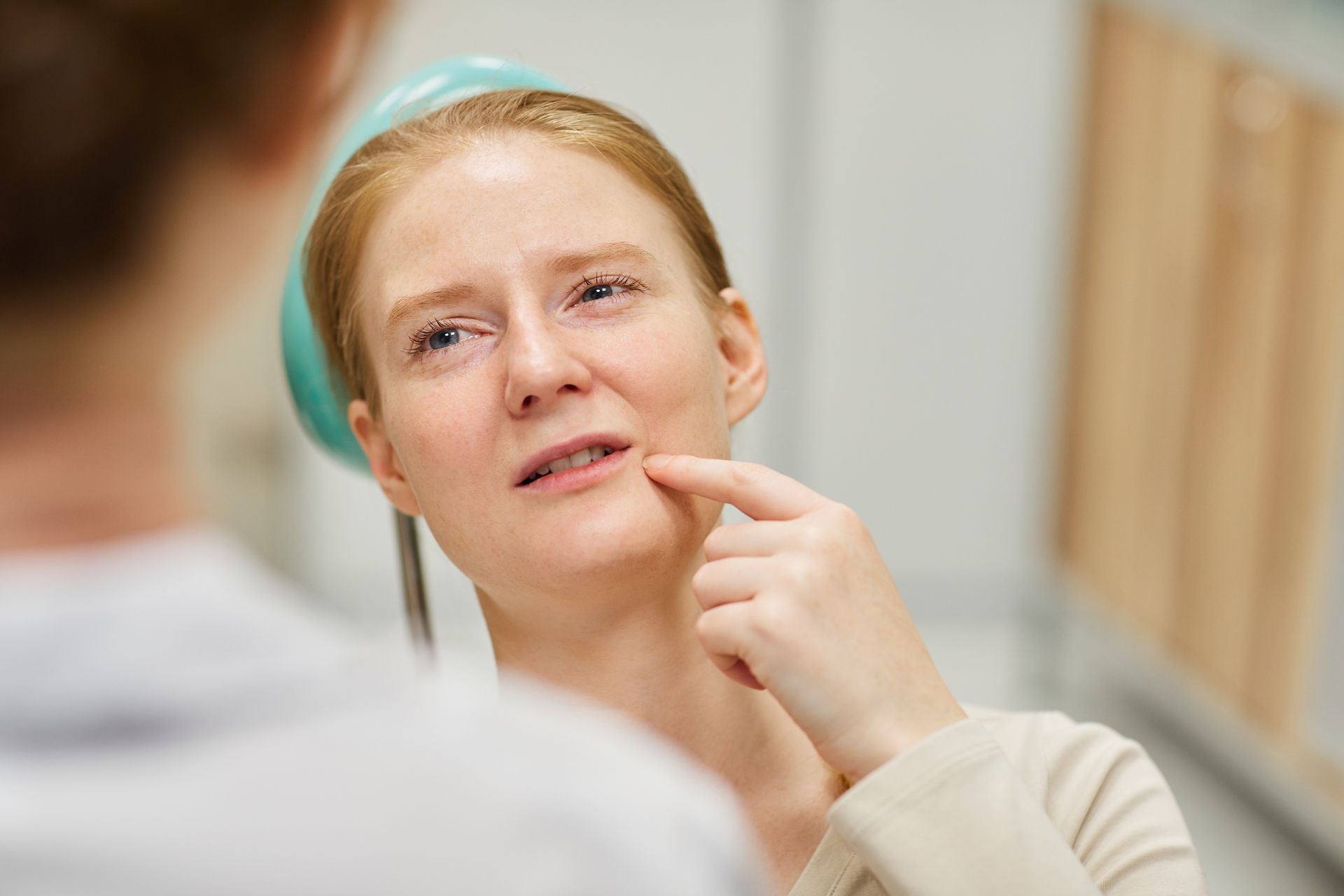 Close-up of a person touching their chin while looking in a mirror, with a concerned expression.