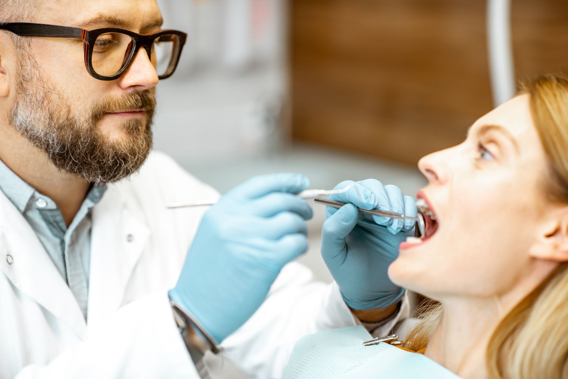 Dentist examining a patient’s teeth with blue gloves and dental tools in a clinic