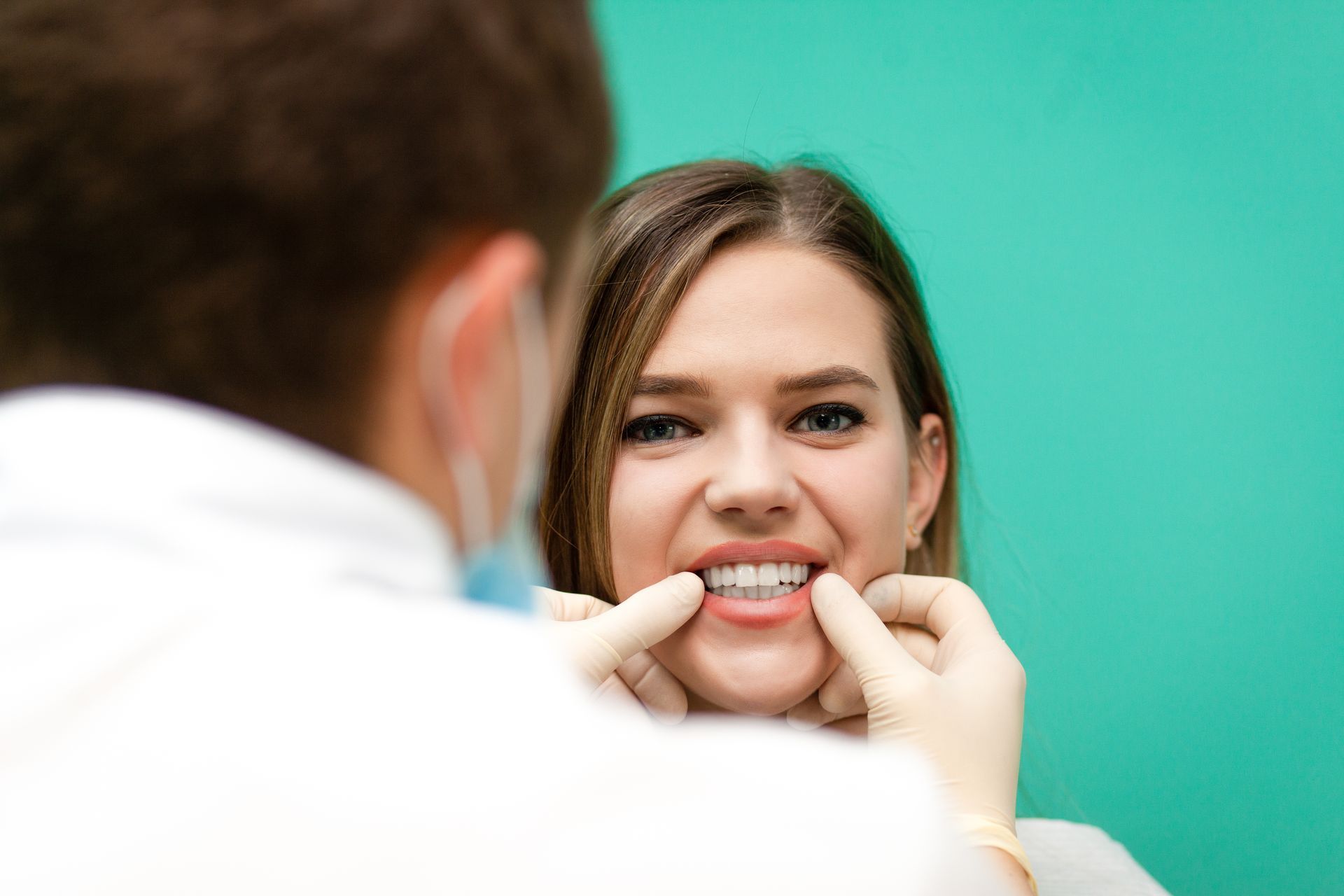 Dentist fitting dental braces on a smiling patient against a teal background