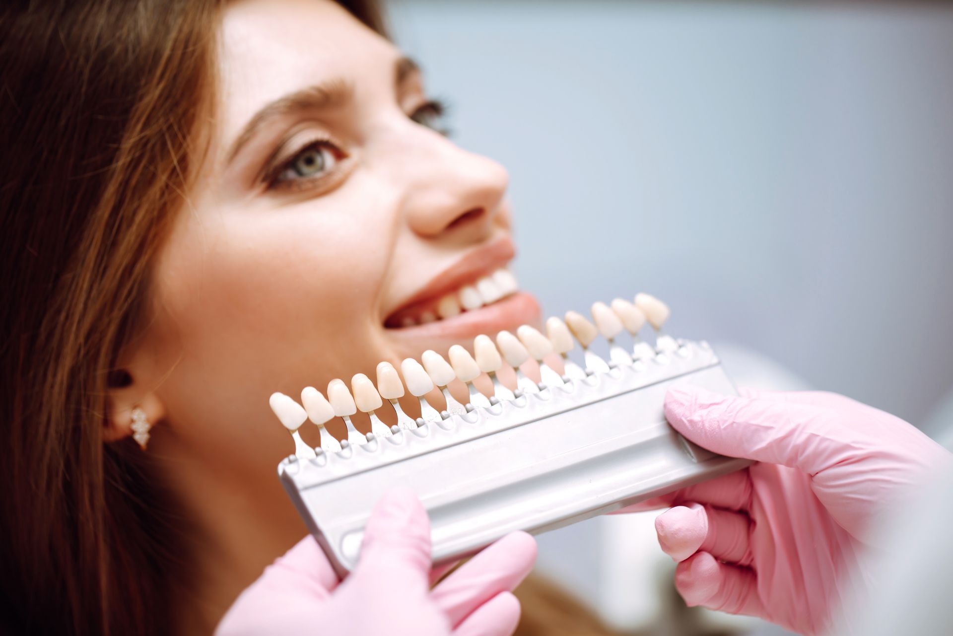 Woman smiling as gloved hands compare dental shade tabs to her teeth