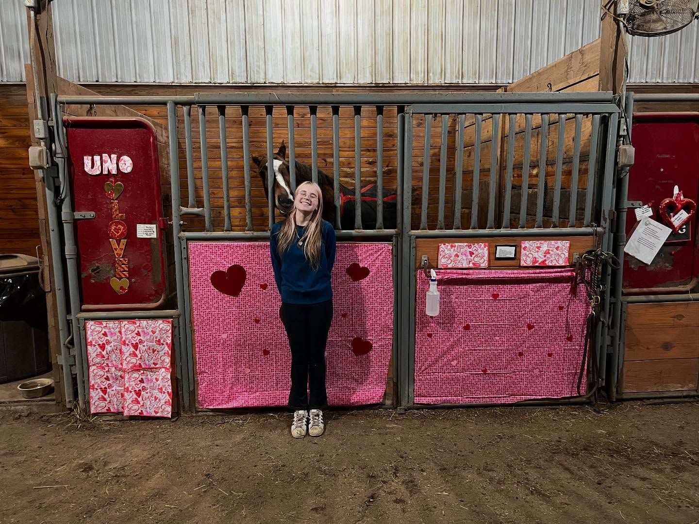 Woman standing in front of a horse stall decorated with pink hearts.