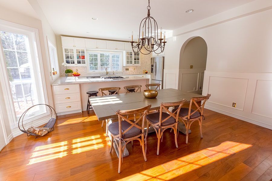 Bright dining room with wooden table, chairs, chandelier, and sunlight streaming across the floor