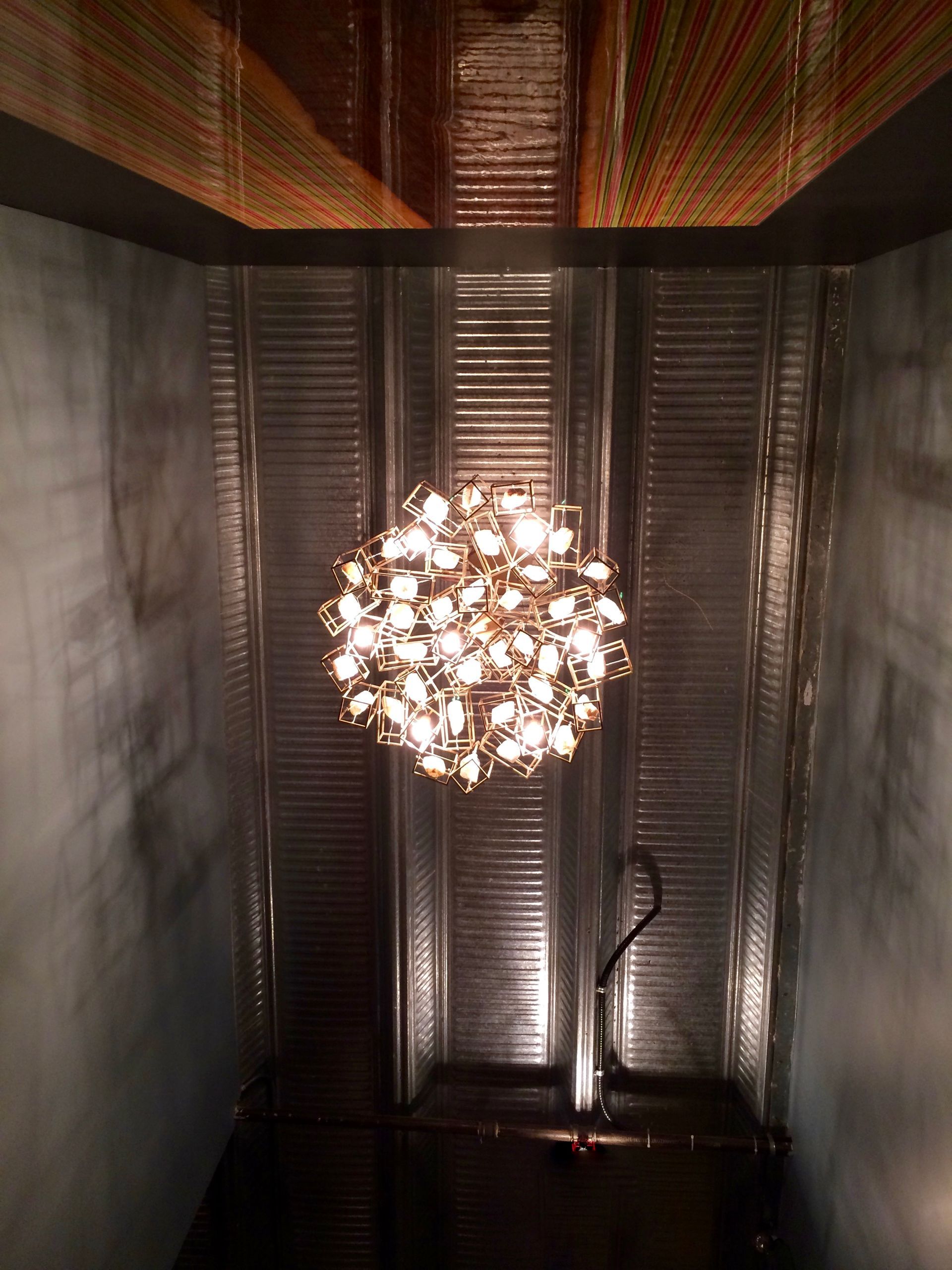 Spherical chandelier glowing in a dark, narrow hallway with textured walls and a striped ceiling.
