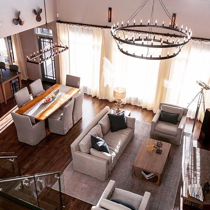 Bright modern living-dining room with gray sofas, wooden table, large windows, and circular chandeliers