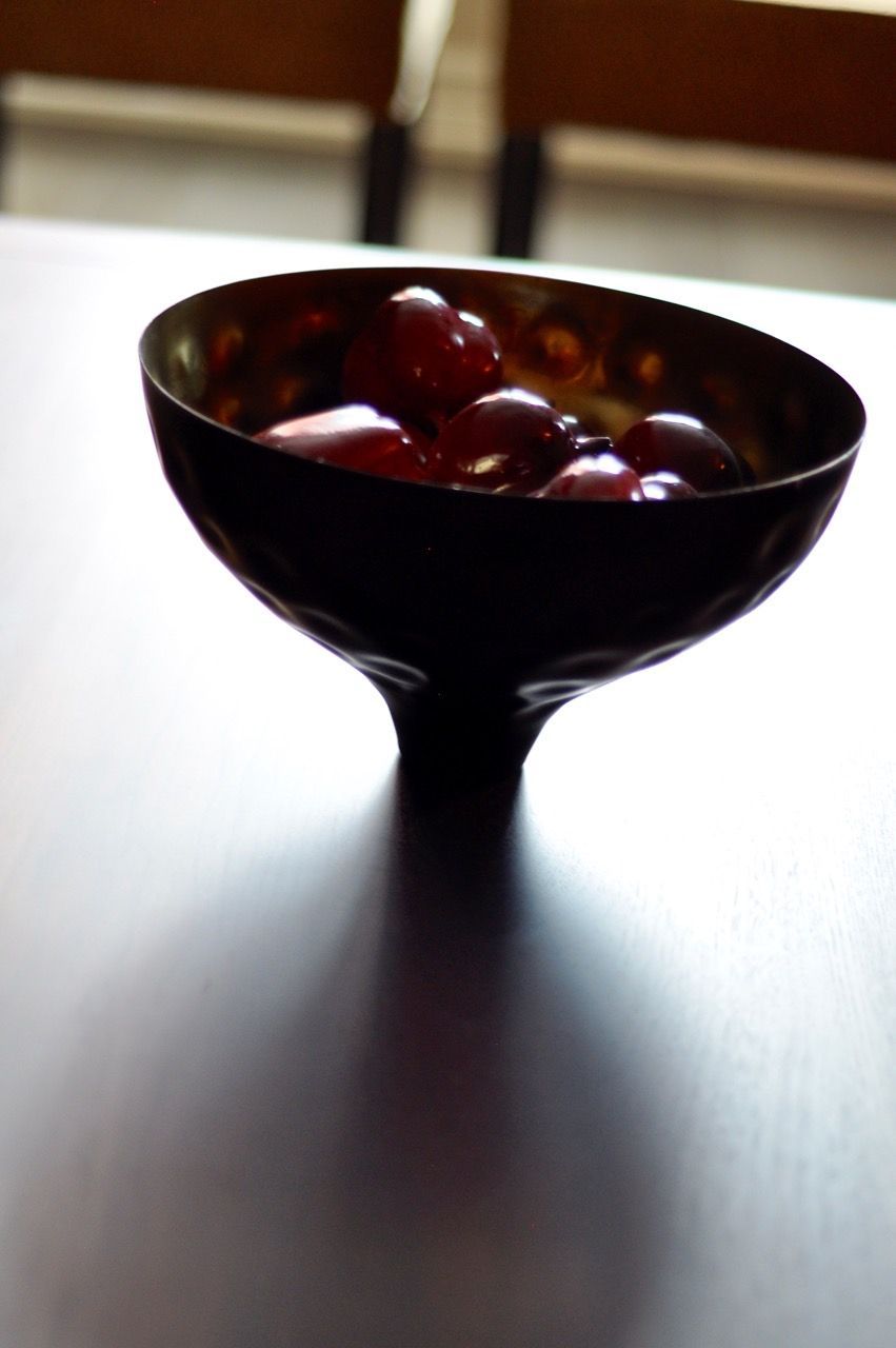 Dark bowl of red grapes on a bright table near a window