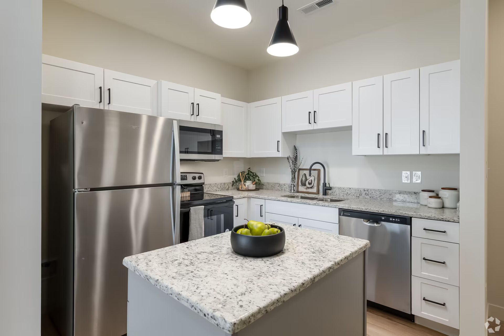 Photo of a kitchen, showing a kitchen island in the foreground and the rest of the kitchen in the background