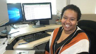 a woman is sitting at a desk with a computer and smiling .