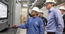 a group of men wearing hard hats and goggles are looking at a computer screen .