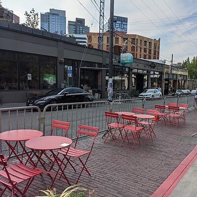 a row of red folding tables and chairs on a sidewalk in front of a building .