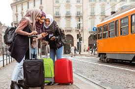 three women are standing on a sidewalk with luggage and looking at a cell phone .