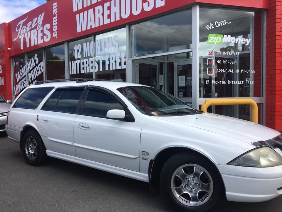 White station wagon parked in front of a tire warehouse with a 