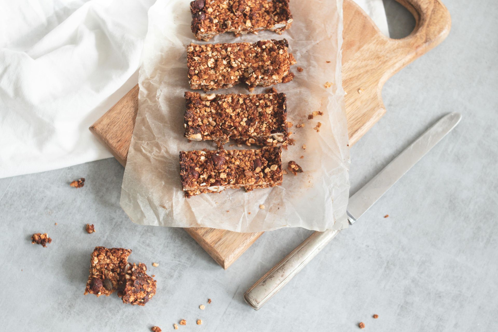 Granola bars on parchment paper, on a wooden board, with a knife and cloth.– holistic recipes