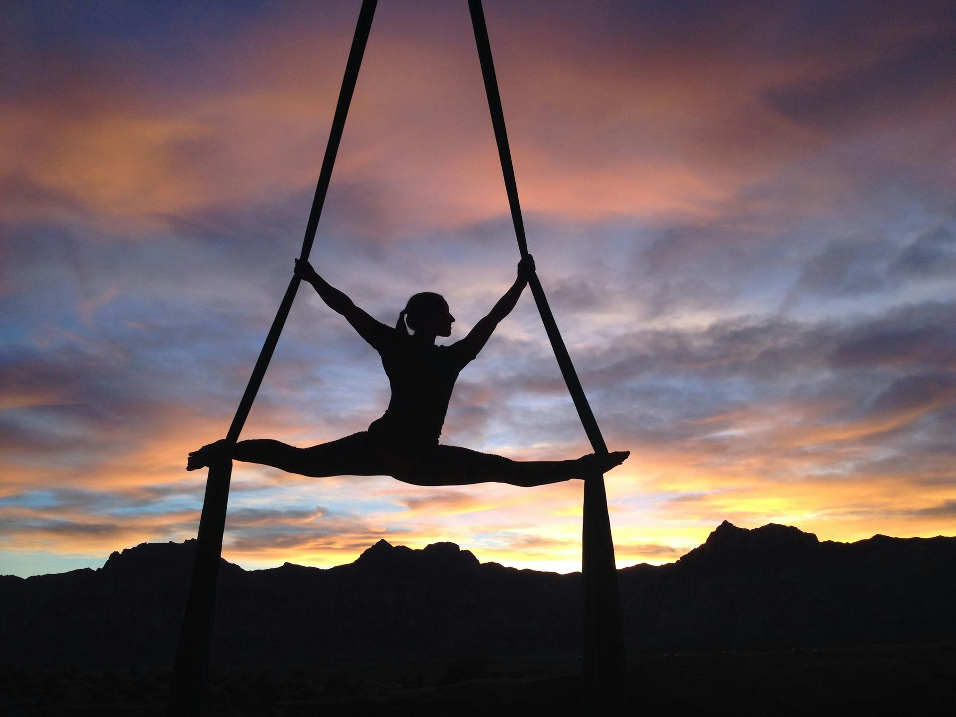 Silhouette of person doing aerial split on silks against sunset.– stress management