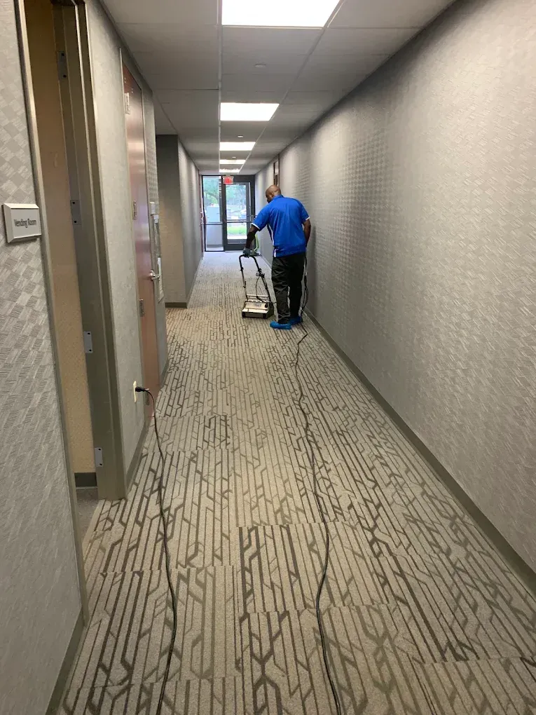 Person cleaning a long office hallway with a carpet machine