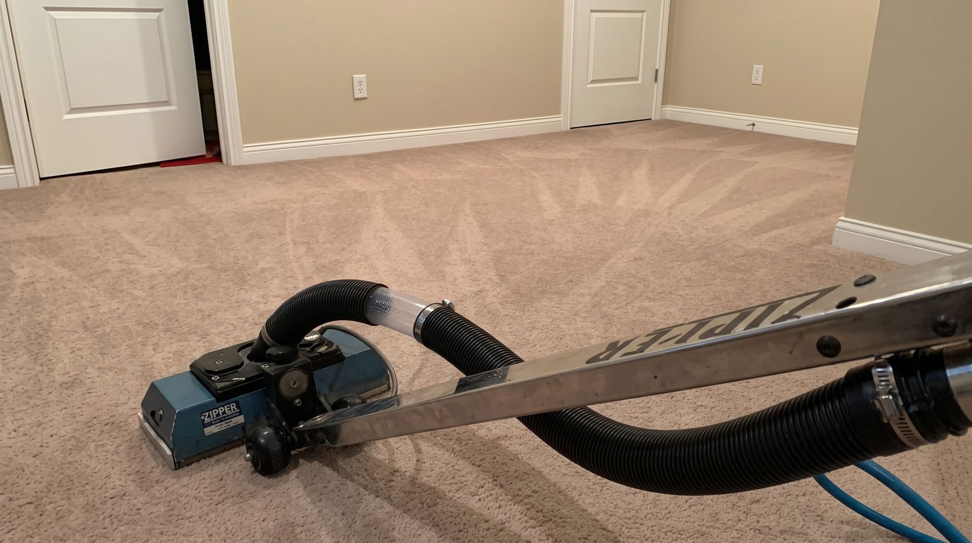 Person pressure-washes a carpeted floor, spraying water and foam in a glass-walled interior.