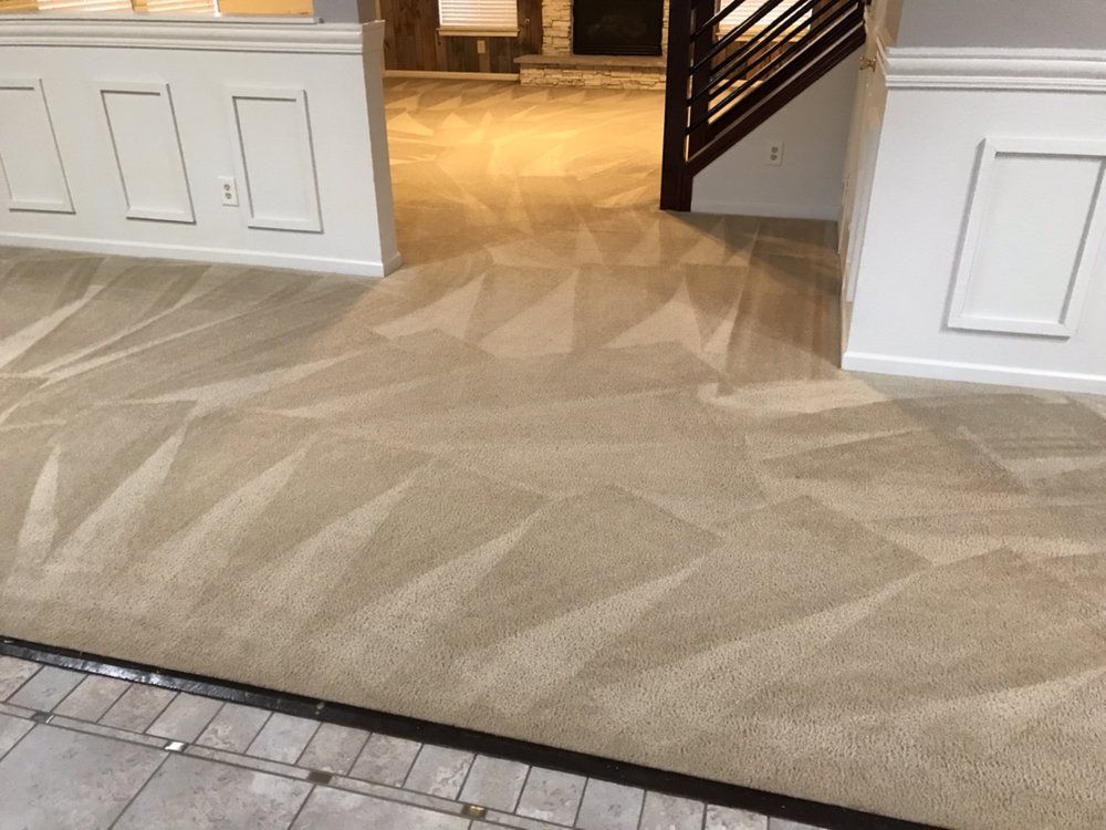 Beige carpeted hallway with geometric pattern leading to a doorway and stairs