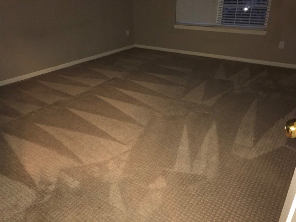 Empty beige carpeted room with geometric pattern, white walls, and a window with blinds.