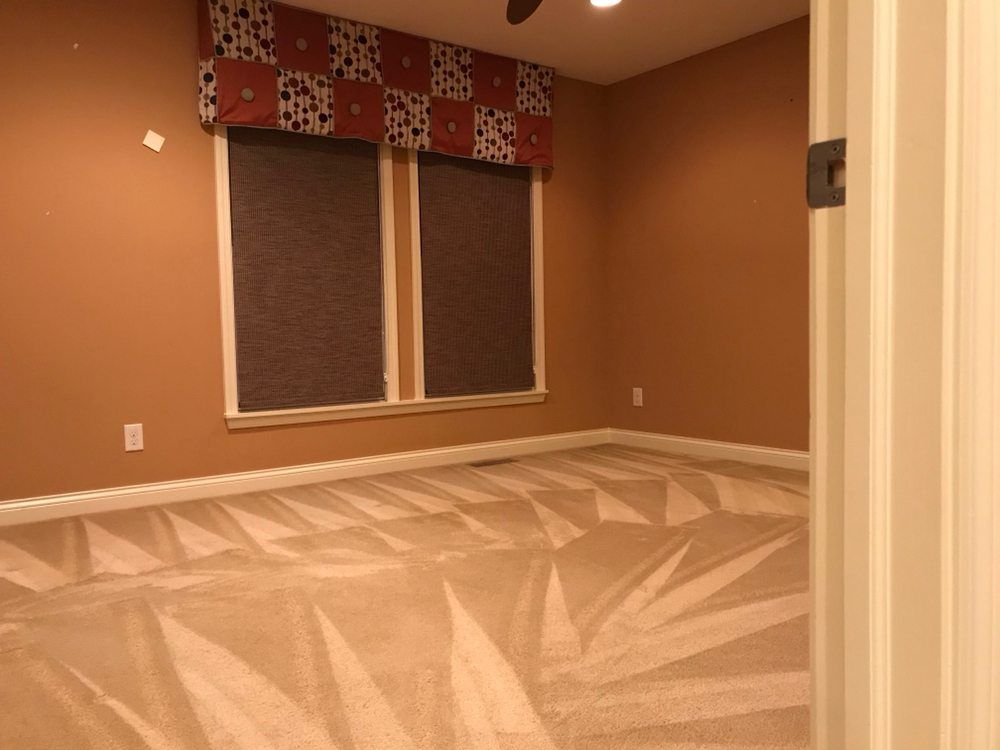 Empty tan room with patterned carpet and two windows with patterned valances