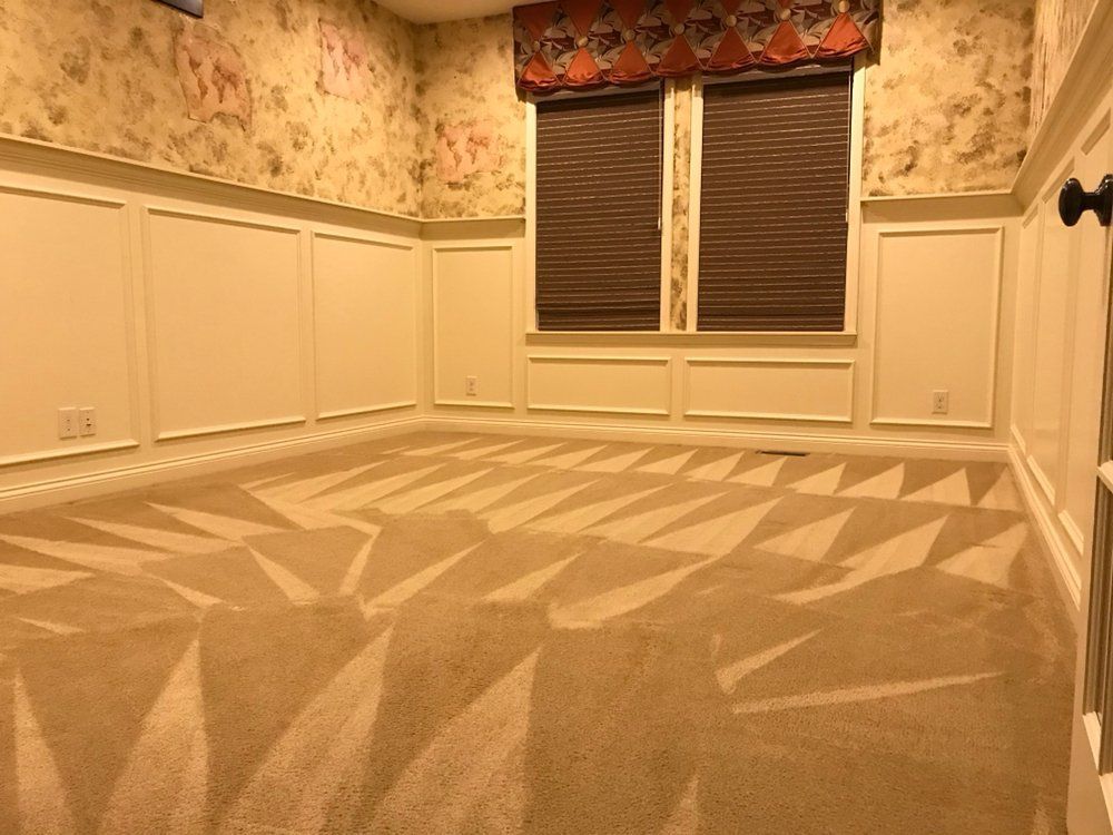 Empty carpeted room with floral wallpaper, white paneling, and two windows with dark blinds and a floral valance
