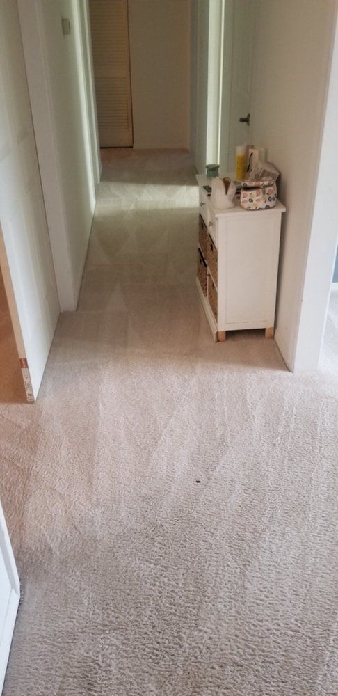 Carpeted hallway with white walls and a small cabinet holding items on the right