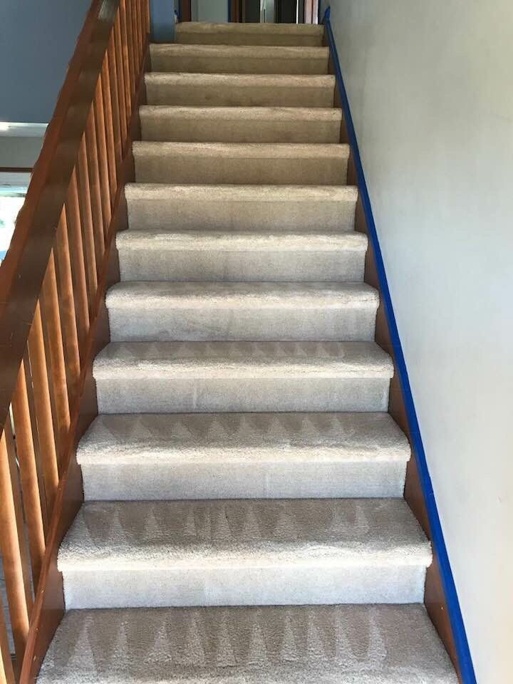 Carpeted indoor staircase with wooden railing and white wall on the right