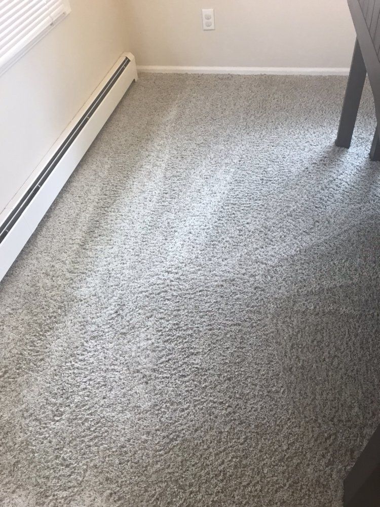 Empty carpeted room corner with baseboard heater and a table leg visible