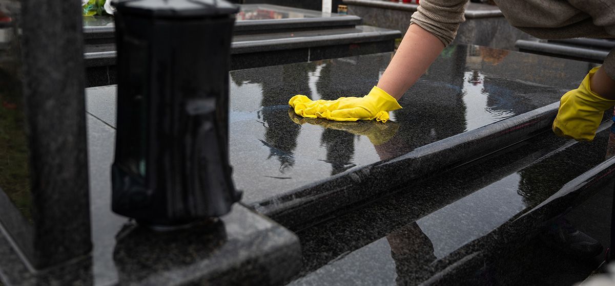 Gloved hands cleaning a wet black railing beside a puddled sidewalk
