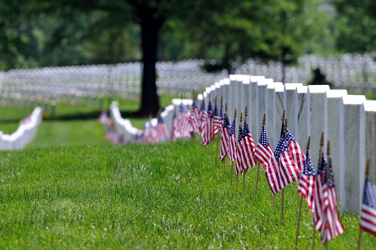 Rows of small American flags beside white cemetery headstones on green grass.