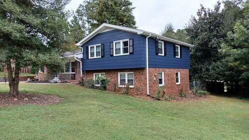A blue and brick house with a large lawn in front of it.