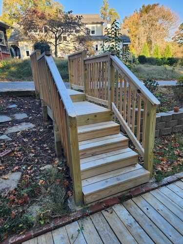A wooden deck with stairs leading up to it and a house in the background.