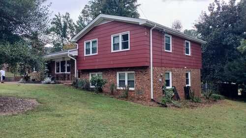 A large red house with a lot of windows is sitting on top of a lush green field.