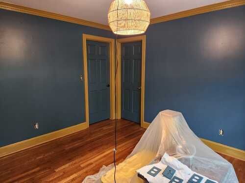 A room with blue walls and wooden floors is being painted.