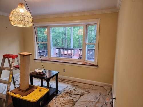 A room with a ladder , table , and window being painted.