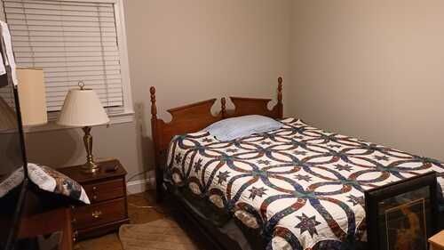 A bedroom with a bed , nightstand , lamp and window.
