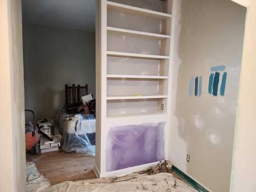 A room with shelves and a door that is being painted.