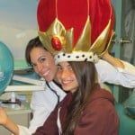 Two people smiling, one wearing a large red and gold crown hat indoors